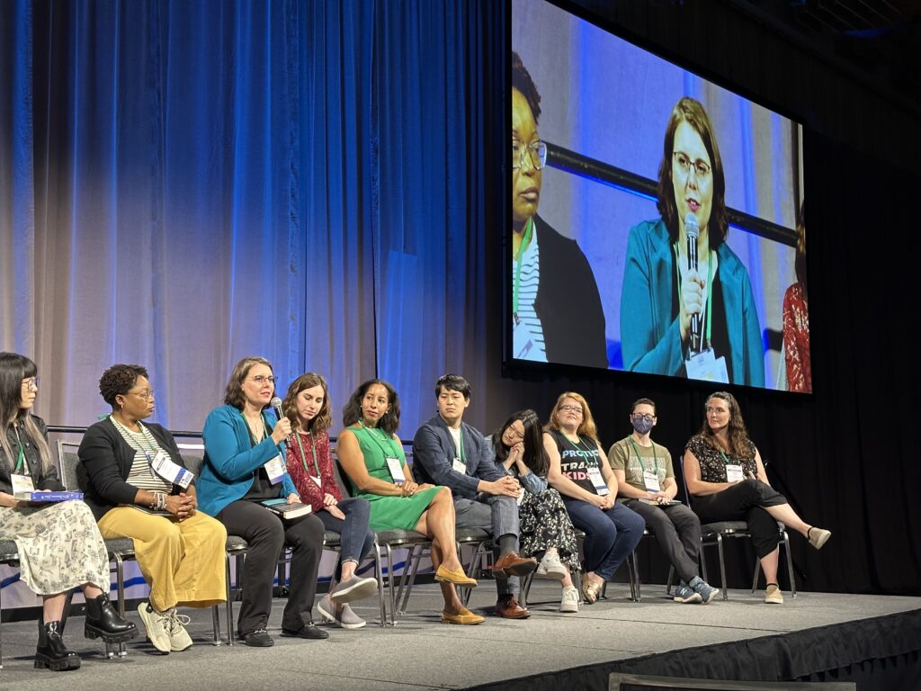 Susan Metallo sits on a stage with other authors speaking into a microphone
