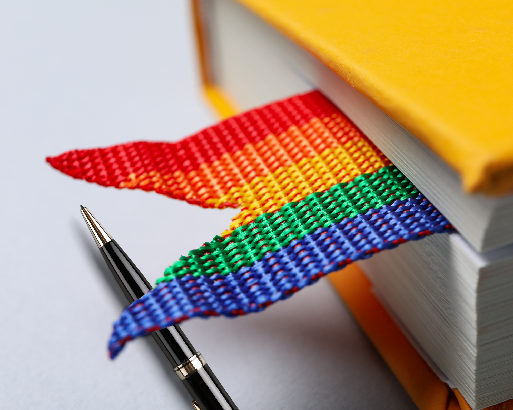 A book with a yellow cover and a rainbow bookmark next to a pen